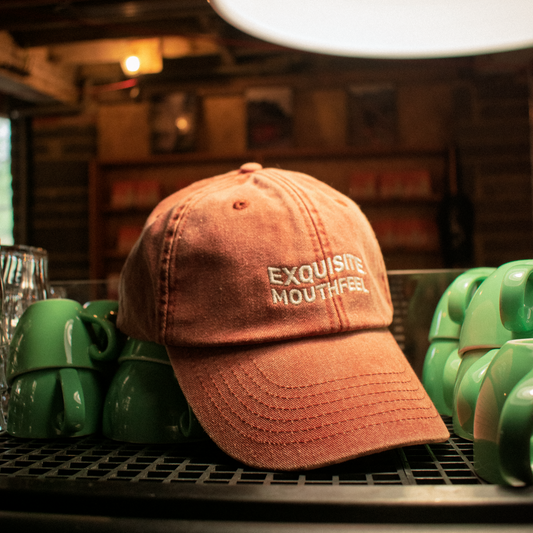 Orange cap with "Exquisite Mouthfeel" embroidered on sitting on top of a coffee machine.